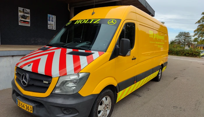 Servicevogn for Holtz folieret af Gylling Skilte – klassisk gul design med røde refleksstriber, der sikrer maksimal synlighed og et rent, professionelt udtryk.