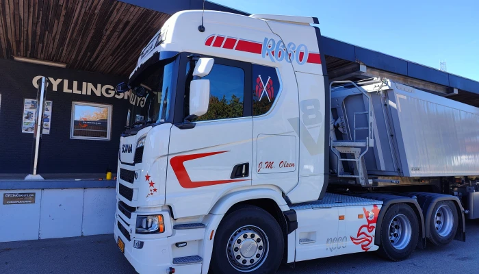 Scania lastbil for J.M. Olsen folieret af Gylling Skilte – flot hvidt design med røde detaljer, der kombinerer styrke, præcision og elegance.